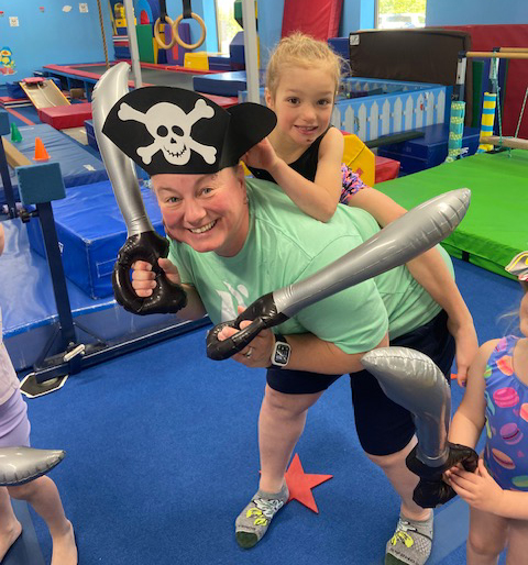 Two kids playing pirates with hats, a sword, and a bat indoors.