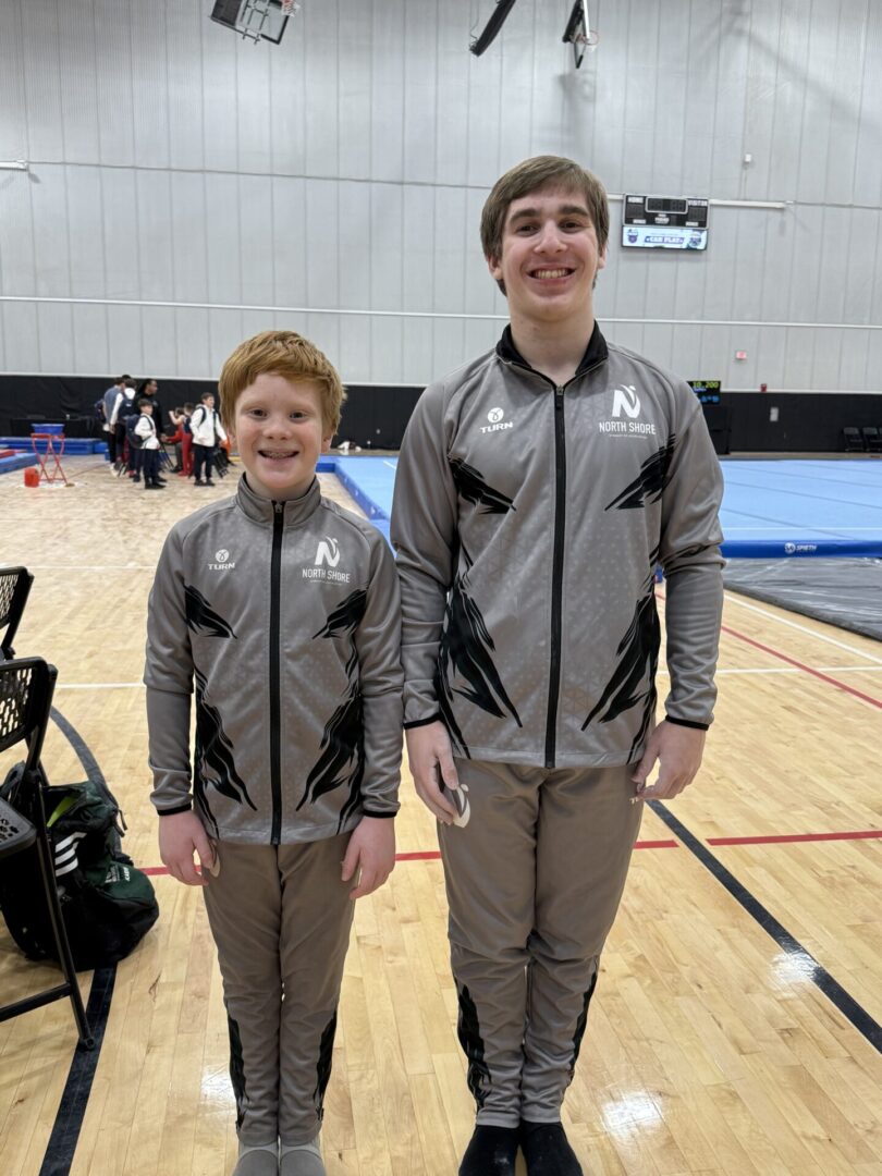 Two boys in matching gray sports jackets standing in a gymnasium.
